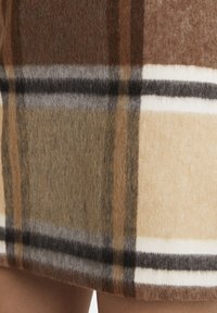 Raibais vilnas audums brūnos, bēšos un olīvzaļos toņos, ar maiņām svītrām krēmkrāsā, pelēkā un melnā krāsā. Mīksta tekstūra un siltā izskats.