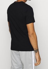 Svart bomulls T-shirt med rund hals och korta ärmar. Slät textur och vanlig passform, visad bakifrån. Inga synliga grafiska element eller mönster.