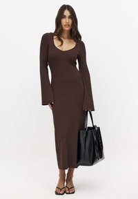 Ruskea ribatut pitkähihaisessa mekossa on syvä V-pääntie, tiukka siluetti ja puoleen säärään ulottuva pituus. Yhdistetty mustan kassi ja sandaalien kanssa.