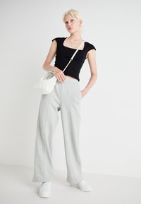 Schwarzes Crop-Top, graue weite Sweatpants, weiße gesteppte Handtasche und weiße Sneakers; glattes Material und lässige Passform, minimalistisches Design.