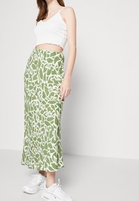 Falda maxi de estampado floral verde con acentos blancos, fabricada en tejido ligero y silueta fluida. Combinada con un top corto blanco y zapatillas blancas.