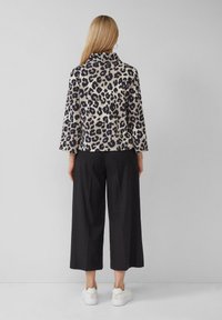 Top a stampa leopardata beige e nera, con collo alto e maniche a tre quarti. Abbinato a pantaloni larghi neri e sneakers bianche.