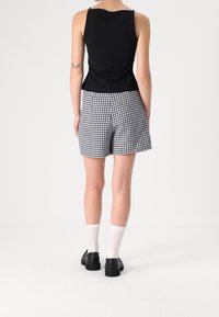 Top nero senza maniche con scollatura tonda, abbinato a pantaloni corti houndstooth bianco e nero a vita alta. Scarpe nere e calzini bianchi.