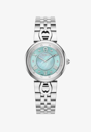 Sudraba metāla pulkstenis ar apļa formu, gaiši zilu mātespērlēm dīli, romiešu cipariem un dimanta akcenta marķieriem. Iekļauj saistītu aproci.