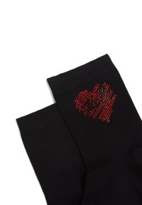 Calze nere con un design testurizzato e accentuate da strass rossi disposti in un motivo su un lato. Materiale morbido con polsini a coste.