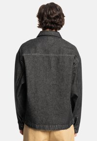 Black denim jacket featuring a relaxed fit, structured collar, and buttoned cuffs. Enhanced stitching detail along the shoulders and hem.