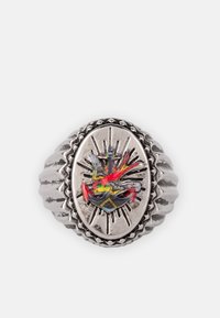 Sølvring med et ovalformet design, tekstureret bånd og et farverigt emblem af en fugl og en solstrålemønster i midten.