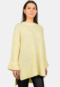 Maglione lavorato a maglia di colore giallo chiaro, con vestibilità ampia, maniche lunghe e polsini a campana. Presenta una texture a coste e un design con orlo dritto e più lungo sul retro.