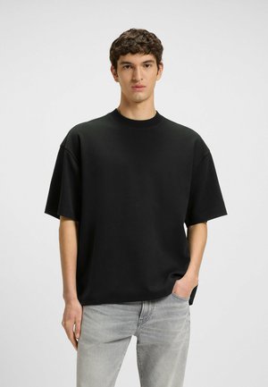 Schwarzes, übergroßes T-Shirt mit kurzen Ärmeln und Rundhalsausschnitt, aus einem weichen Stoff, kombiniert mit hellgrauen Jeans. Schlichtes, einfaches Design.