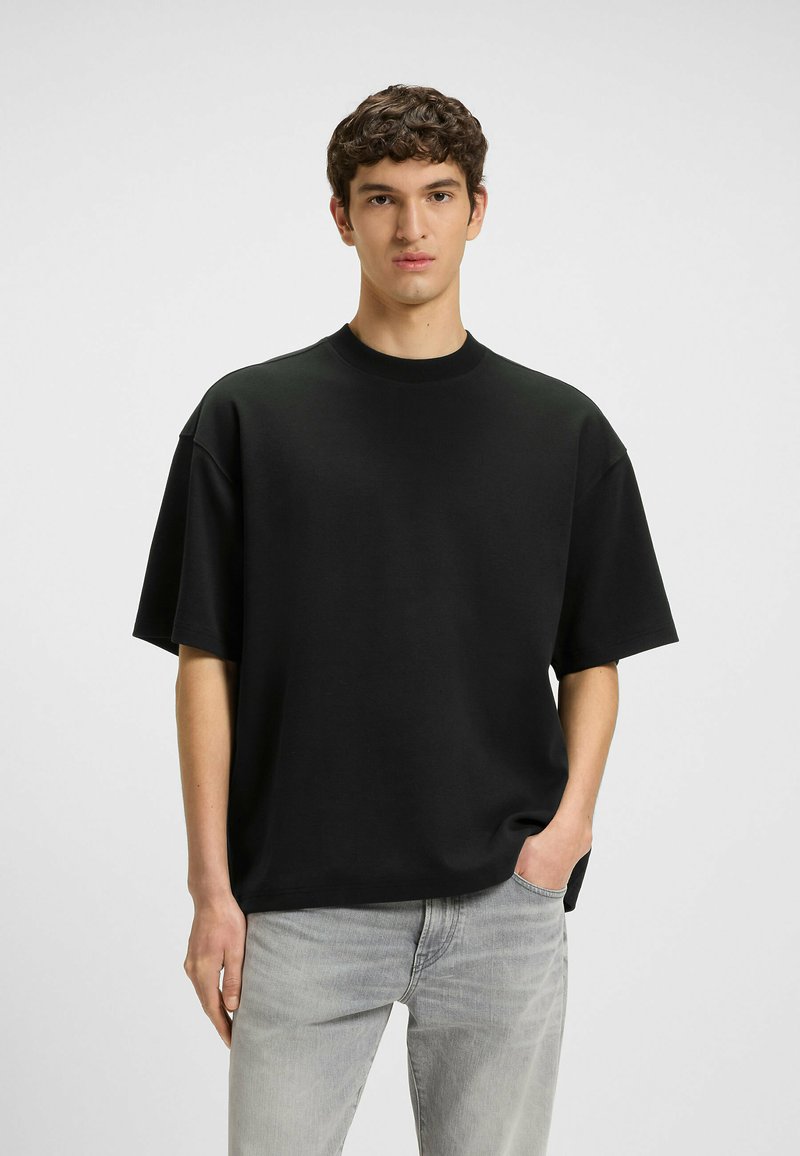 Black oversized short-sleeve t-shirt with a crew neckline, made from a soft fabric, paired with light grey jeans. Clean, simple design.