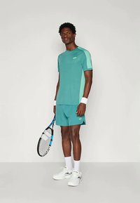 Teal idrottströja med ljusare teal detaljer och logotyp, i kombination med matchande shorts. Inkluderar tennisracket, vita strumpor och skor.