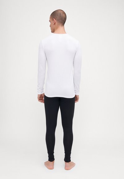 Weißes Langarmhemd und schwarze enge Leggings, die eine glatte Textur und ein minimalistisches Design zeigen, von hinten vor einem neutralen Hintergrund betrachtet.