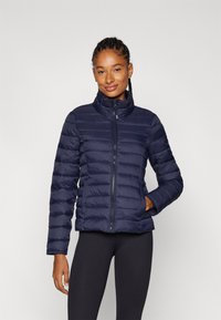 Manteau en duvet bleu marine avec un col haut, un design à couture verticale et une fermeture éclair. Dispose de poches avant et d'une texture lisse et isolante.