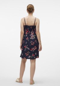 Abito estivo floreale con sfondo blu navy, spalline sottili regolabili, arricciature elastiche sul retro, orlo fino al ginocchio, tessuto morbido.