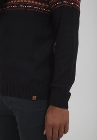 Gestrickter Pullover in dunklem Marineblau mit mehrfarbigem gemustertem Einsatz, gerippten Bündchen und Saum, einschließlich eines kleinen Lederetiketts am Boden.
