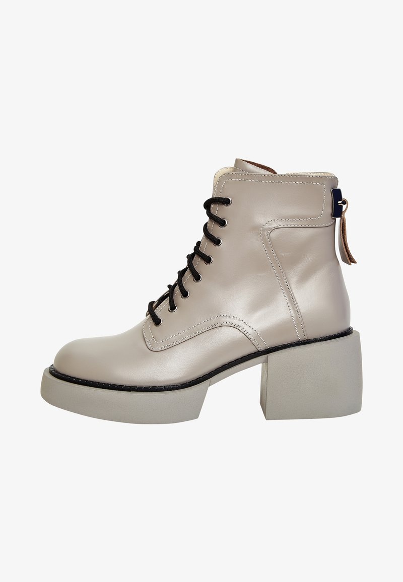 Bottine beige en cuir avec lacets noirs, talon bloc épais et languette à l’arrière, photographiée sur fond blanc.