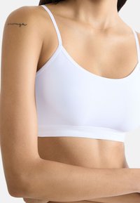 Witte, rekbare bralette met dunne, verstelbare bandjes en een glad, naadloos ontwerp. Beschikt over een zachte textuur en een aansluitende silhouet.