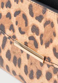 Pochette en imprimé léopard fabriquée en matériau texturé de couleur brun clair avec des taches foncées. Présente une bande d'accent métallique dorée.