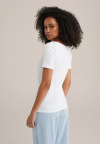 Tricou alb, ajustat, cu mâneci scurte, decolteu rotund și textură netedă, asortat cu pantaloni călcați cu dungi albastre deschise.