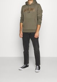 Oliwkowa zielona bluza z kapturem, z kieszenią kangura i sznurkiem, z logo "JACK & JONES". W zestawie z ciemnymi dżinsami i czarnymi trampkami.