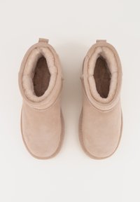 Beige suède enkellaarzen met een zachte fleece voering, ronde vorm, gestikte accenten en een achter tabs voor gemakkelijk aan- en uittrekken.