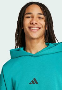 Tyrkysová mikina s kapucňou a prednou klokaniou vreckom, s čiernym logom v podobe troch pruhov na hrudi. Materiál vyzerá hladko a ľahko.