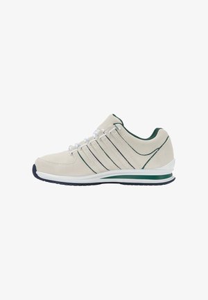 Beżowe buty sportowe z zamszową cholewką, zielonymi akcentami i trzema ciemnymi paskami. Posiadają białą podeszwę środkową i gumową podeszwę zewnętrzną dla lepszej przyczepności.