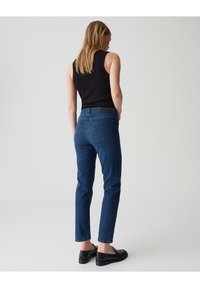 Jean en denim bleu foncé avec une coupe droite, taille mi-haute et poches arrière discrètes. Associé à un haut sans manches noir et des mocassins.