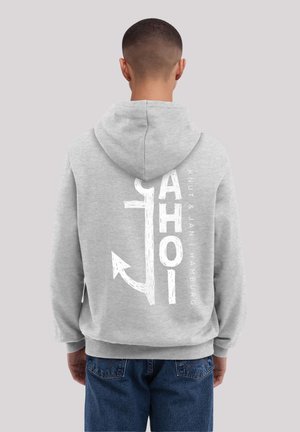 Person wearing gray hoodie with large white anchor graphic and "AHOI" text on back, paired with blue jeans, standing against plain background.