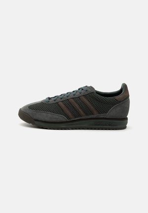 Grijze Adidas-sneaker met mesh- en suède panelen, drie donkere strepen en een textuurrijke zool, zijaanzicht tegen een witte achtergrond.