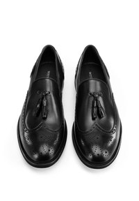 Zapatos de cuero negros con detalle de borlas, diseño de punta de alas, patrón perforado y acabado suave. Punta redondeada y suela de perfil bajo.