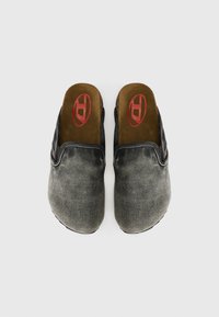 Zwarte instapschoenen met een vervaagde denimtextuur, bruine binnenvoering en een rode logo bij de tenen. Platte zool met gebogen randen.