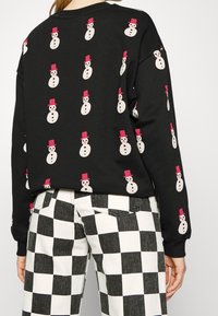 Felpa nera con grafiche ripetute di pupazzi di neve con cappelli rosa. Abbinata a pantaloni a scacchi bianchi e neri. Design casual e confortevole.