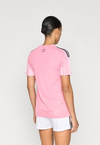 Világos rózsaszín rövid ujjú sportpóló fekete részletekkel és hálós textúrával. "Freedom to Dream" felirat a hátsó galléron.