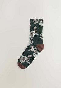 Mørkegrøn sok med brun hæl og tå, dekoreret med hvide og brune blomstermønstre, lagt fladt på en lys baggrund.