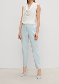 Blouse blanche sans manches à col cheminée associée à un pantalon bleu clair cintré et à des chaussures à talons assorties ; tissu lisse et coupe ajustée.