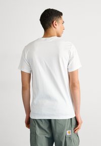 T-shirt bianco in cotone con colletto rotondo e maniche corte. La parte posteriore presenta una texture liscia, senza loghi o motivi visibili.