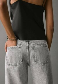 Črna brezrokavnik kombinirana s svetlo sivo visokim pasom hlačami, ki imajo dve zadnji žepki in rahlo zbledelo teksturo.