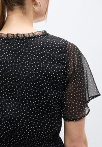 Μαύρο φόρεμα με πουά, διαφάνεια στα κοντά μανίκια, στρογγυλή λαιμόκοψη με δαντελένιο τελείωμα και ζώνη στη μέση που δίνει κολακευτική γραμμή.