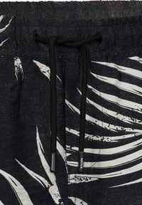 Czarne szorty w biały wzór palmowych liści, z elastycznym paskiem w talii i czarnym sznurkiem. Materiał wydaje się lekki i teksturowany.