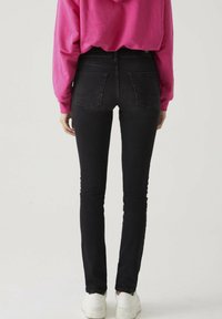 Zwarte skinny jeans met een hoge taille, achterzakken en een gladde, rekbare stof. Draag ze met een roze hoodie en witte sneakers.