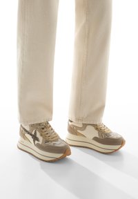 Sneaker platform beige con stampa effetto serpente texturizzata, dettagli in crema liscia e chiusura stringata tonale. Indossate con pantaloni chiari e morbidi.