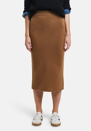 Strickrock in Braun, midi-lang, mit einem gerippten Bund, gerader Form und strukturiertem Stoff, kombiniert mit weißen Turnschuhen und einem schwarzen Pullover.