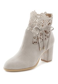 Beige Knöchelstiefel aus Kunstwildleder mit Spitzenverzierung oben, mit einem Band gebunden, und einem dicken Absatz. Glatte Textur und spitze Zehen.