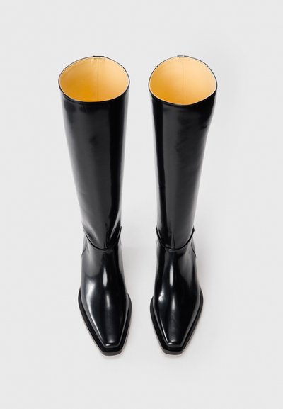Knee-high mustad mustast nahkkingad läikiva viimistlusega, ruudukujulise nina ja kontrastses kollases sisevoodis. Omab stiilset, minimalistlikku disaini.