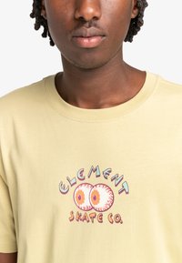Lichtgele katoenen t-shirt met een kleurrafische afbeelding met ogen en de tekst "ELEMENT SKATE CO." in retro stijl. Standaard ronde hals.