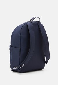 Navy blue backpack with padded straps, side pocket, and branded loop handle, standing upright on a white background.