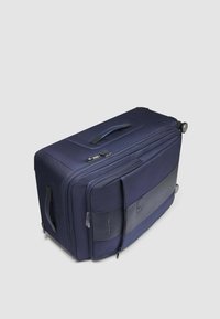 Marineblaue Reisetasche aus strukturiertem Polyestergewebe, mit zwei Rollen und einem Tragegriff oben. Verfügt über eine vordere Reißverschlusstasche und ein kontrastierendes Lederpaneel.