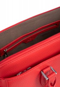 Interno di una borsa in pelle rossa con una tasca con zip, fodera marrone e esterno testurizzato. Presenta un dettaglio in metallo e cuciture decorate.