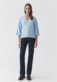 Lyseblå oversized sweater med V-hals, trekvartærmer, ribbet kant, parret med mørkeblå jeans og brune sko.